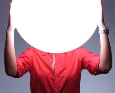 young casual woman covering her ears over a shiny blank circle. hear no evil concept. on gray background